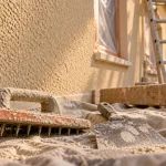Enduit gratté : taloche et gratton sur mur de façade en chantier